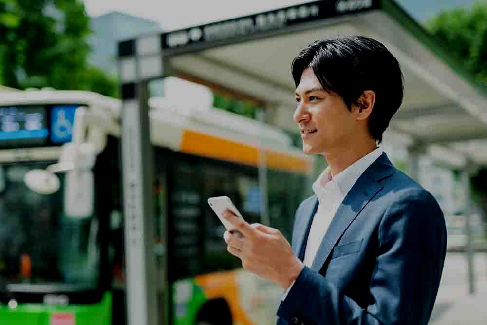 のんびりデザインオフィスのトップページを飾るグラフィックイメージ（バス停の前でスマートフォンを使ってお客様と笑顔でコミュニケーションする若い男性）